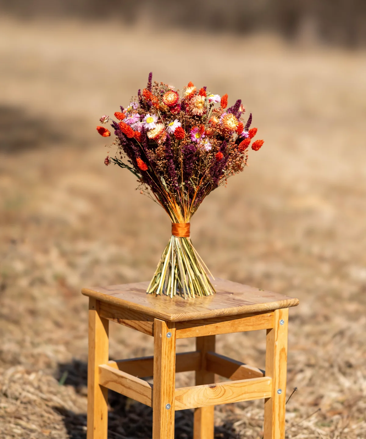Kytica zo sušených kvetov Červené zore v červených a oranžových tónoch na drevenej stoličke